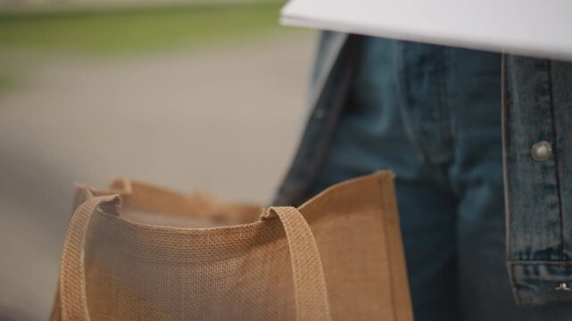 Urban message exchange. Person placing letter into tote during errands. Close shot of hand inserting envelope into bag scene. Scene of person carefully inserting letter into bag amidst city errands
