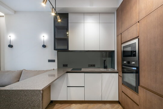 A modern kitchen is shown in a cozy apartment. The kitchen features a sleek design with simple cabinets, a countertop, and built-in appliances. The space is well-lit and functional