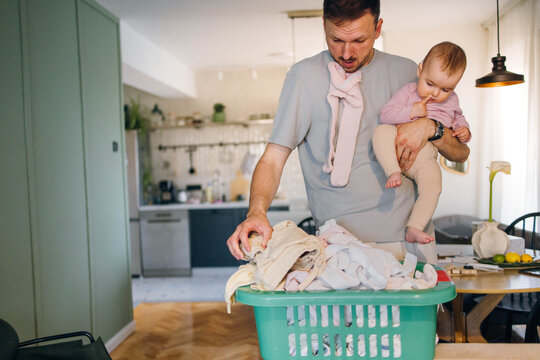 Busy dad talking on the phone carrying laundry basket and baby