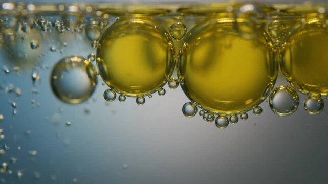 Macro shot of bright yellow oil droplets floating in water with a gradient blue and gray background