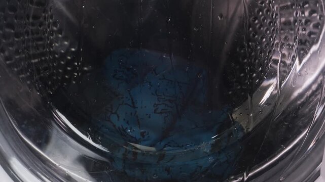The washing machine is washing clothes, the drum is spinning. Medium shot.