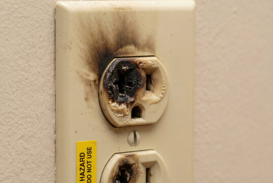 Burned electrical outlet with scorch marks, melted plastic, fire hazard, close-up electrical failure concept