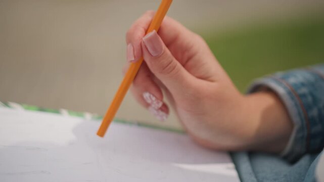 Detailed hand sketching under natural sunlight. Artistic hand rendering of pencil marks outside in daylight. Closeup view of hand meticulously sketching with pencil on paper outdoors in natural light