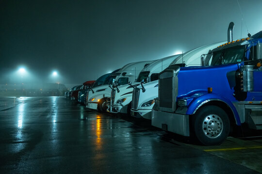 Row of blue semi trucks parked at night with headlights on