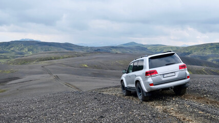 Fototapeta premium Off-road SUV driving through volcanic highlands landscape in Iceland under dramatic sky