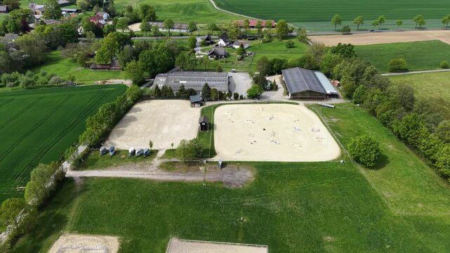 Drone footage shows an equestrian center with riders practicing show jumping in a rural setting
