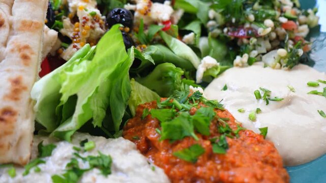 Colorful and healthy mediterranean appetizer platter featuring a variety of salads and dips like hummus, muhammara, and baba ghanoush, served with fresh pita bread for a wholesome vegan meal