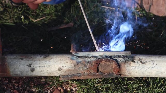 A welder is performing arc welding on an iron pipe in an open area