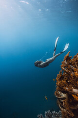 Naklejka premium Woman freediver dives underwater near coral reef