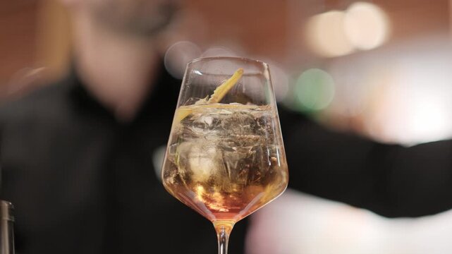 Refreshing chilled cocktail with ice and a lemon garnish in a glass against a blurred bar background