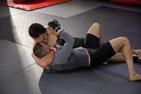 MMA pair grappling on mats, one locking headlock seeking tap, other defending, motion lines on grip