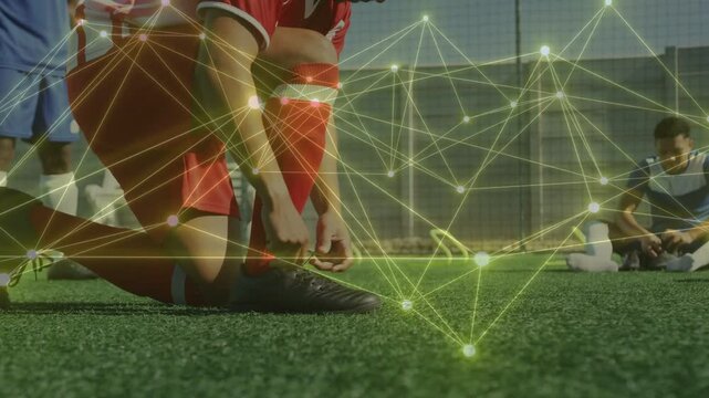 Kneeling red-kit player tying cleat on turf before play, node network tracking footwork for sports