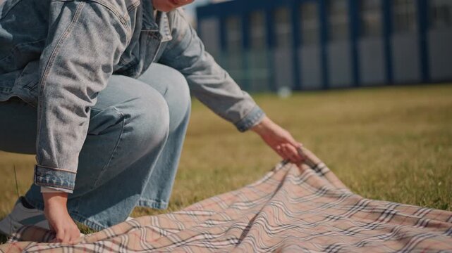 Sunlit scene with woman adjusting blanket. Woman carefully straightening plaid blanket on grassy lawn. Intimate moment of woman smoothing checkered blanket on bright sunlit grass field