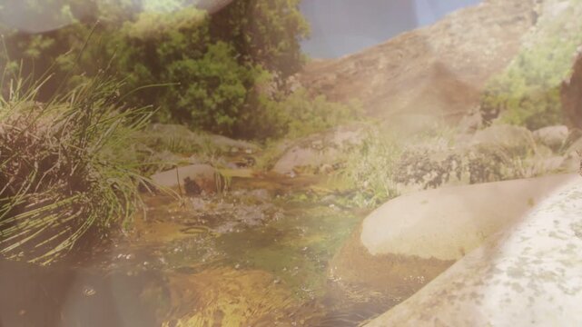 Sun striking water causing spark, rocky stream flowing as cam pulling back, rising, revealing hill