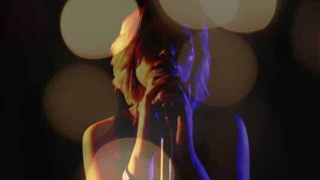 Female singer lowering hands, bringing mic near, starting singing on music stage with bokeh veil