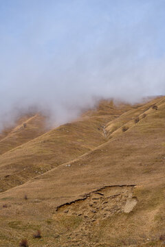 Misty rolling mountain hills with dry golden grassland, atmospheric highland landscape shaped by erosion and low clouds