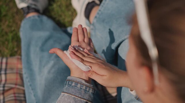 Napkin on hands during picnic closeup, young woman in denim jacket sitting on plaid blanket wipes hands after snack with warm grass and sunlight, intimate leisurely moment with texture and movement