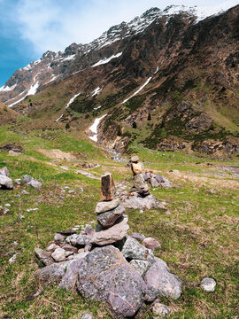 Zen stone cairn on a hiking trail in the high mountains with snow-capped peaks and green valley background at Diga di Gleno.