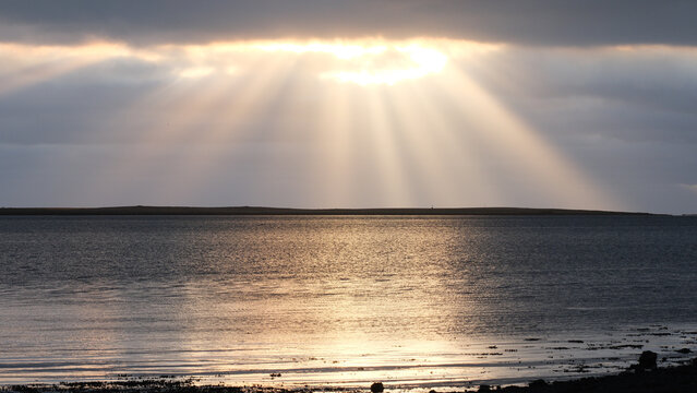 Dramatic sun rays shining through clouds over a calm ocean surface with golden reflections, creating a peaceful and atmospheric seascape.