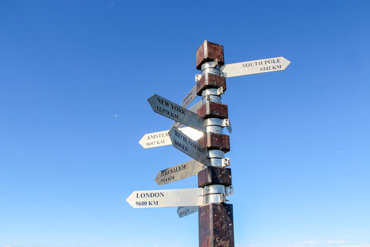 Direction signpost pointing world cities blue sky background. Metal arrows indicating global travel destinations distance during sunny day suitable for tourism and adventure navigation concepts