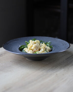 Fagotti ravioli ripieni di pera e gorgonzola, serviti con rucola e noci in stile fine dining su piatto azzurro con luce soffusa