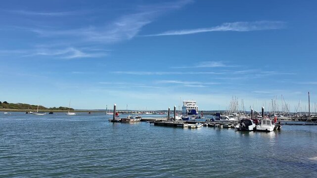 Lymington Hampshire England UK. Video. An Isle of Wight  passenger and vehicle ferry on the Lymington river bound for the IOW passing small boats on pontoone in mid stream.