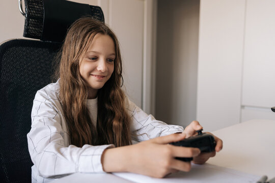 Young girl enjoying video gaming at home, holding controller and smiling while immersed in recreational digital entertainment and modern leisure activity.