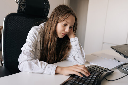 Teenager girl learning online, concentrating on computer tasks, gaining knowledge in home office environment, engaged in remote education and digital studies.