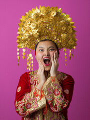 Naklejka premium Surprised Young Indonesian Asian Girl Wearing Ornate Gold Headdress And Embroidered Traditional Costume On Pink