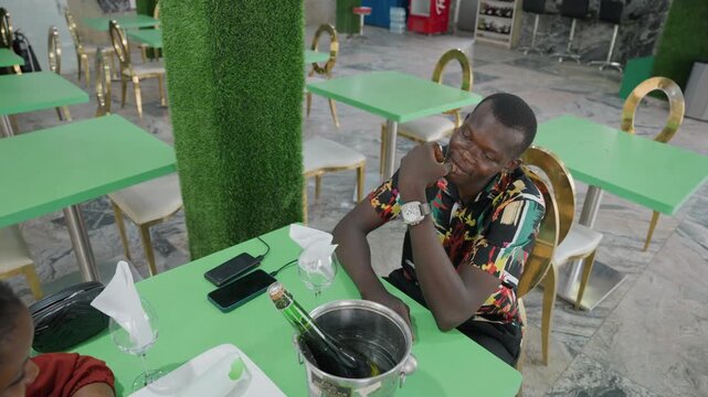 Relaxed man enjoying city cafe ambiance. Adult male with colorful attire relaxing at outdoor eating spot. Casual man with bright clothing and thoughtful expression at street cafe during evening