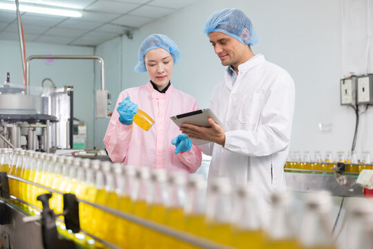 Two workers in a beverage factorydiscuss behind the juice bottle production line