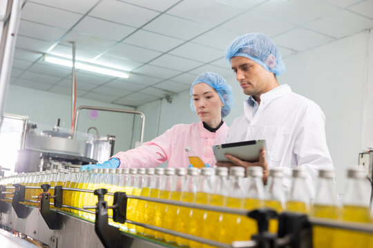 Two workers in a beverage factorydiscuss behind the juice bottle production line