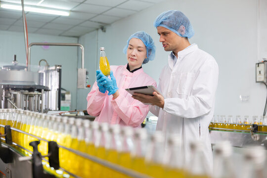 Two workers in a beverage factorydiscuss behind the juice bottle production line