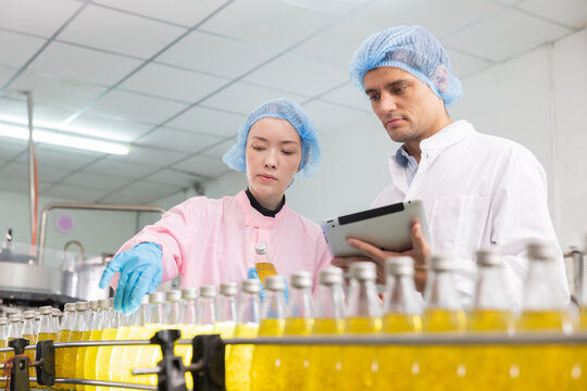 Two workers in a beverage factorydiscuss behind the juice bottle production line