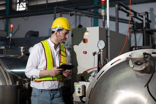Worker stands in a factory with machinery while holding a tablet in hand