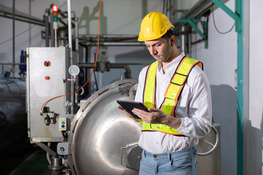 Worker stands in a factory with machinery while holding a tablet in hand