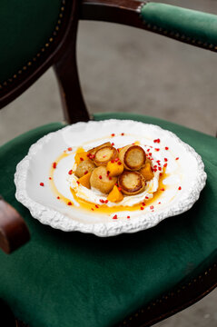 Gourmet plating of pan-seared scallops or dumplings with roasted pumpkin and yogurt sauce on a white textured plate, set on a green velvet vintage chair.
