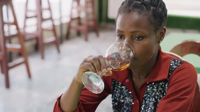 Black woman sipping wine in restaurant, on romantic date night, staring into glass with pensive expression, waiting for companion, soft warm lighting and intimate bistro atmosphere, empty chairs