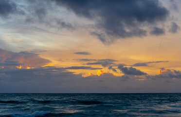 Fototapeta premium Sunset over the ocean with dramatic clouds in Miami. Dark sea waves under a colorful sky with orange light breaking through gray clouds at dusk in Miami, Florida.