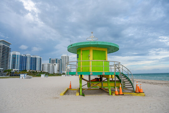Lifeguard station on beach with city skyline background. Green and yellow rescue tower on sand with high rise buildings and cloudy sky in Miami.