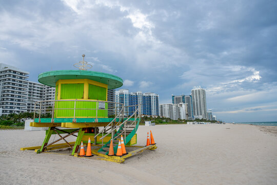 Lifeguard tower on wide sandy beach under cloudy sky. Iconic colorful rescue station on empty Miami Beach with ocean and skyline in distance.