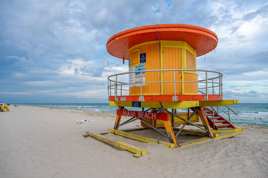 Colorful lifeguard tower number sixty on Miami Beach sand. Close up of a yellow and orange wooden lifeguard station with ocean waves and coastal horizon in Florida.