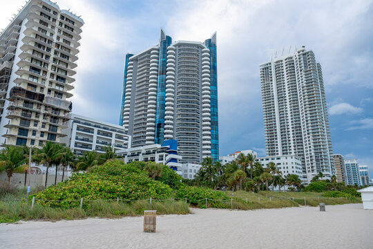Luxury high rise buildings and sand dunes in Miami Beach. View of modern apartment towers from the beach with tropical vegetation and sand under a cloudy sky.