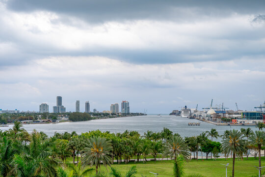 Panoramic view of PortMiami waterway and Miami Beach skyline. Wide shot of the channel leading to the Atlantic Ocean with palm trees and port infrastructure.