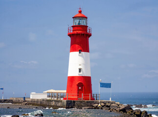 Fototapeta premium A red and white lighthouse standing tall on a rocky coastline, surrounded by natural beauty