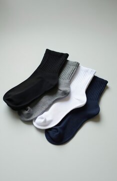 Four pairs of mens socks in different colors black grey white and blue lie on a light gray background. Cotton socks are arranged diagonally, showing ribbed cuffs. Each pair is clean and neatly folded.