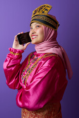 Naklejka premium Smiling Woman in Pink Hijab and Traditional Southeast Asian Costume Talking on Phone