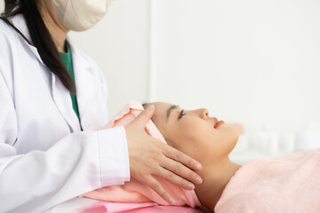 Naklejka premium Woman relaxes with closed eyes during a facial treatment. Practitioner gently adjusts her face with precise fingers. Her smile reflects calm and pleasure from the care 