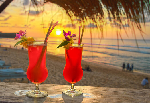 Tropical red cocktails in a beach bar at sunset with flower and straw decorations