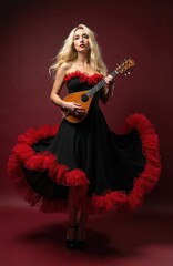 Fototapeta premium Woman in black dress with red ruffles holds mandolin. Blonde plays acoustic instrument studio portrait. Elegant female musician pose, elegant flamenco dress.